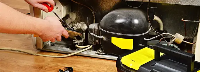 Refrigerator repair technician fixing the compressor and wiring in Braddock, PA