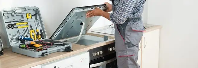 Cooktop repair technician lifting a built-in stovetop for service in Pittsburgh, PA
