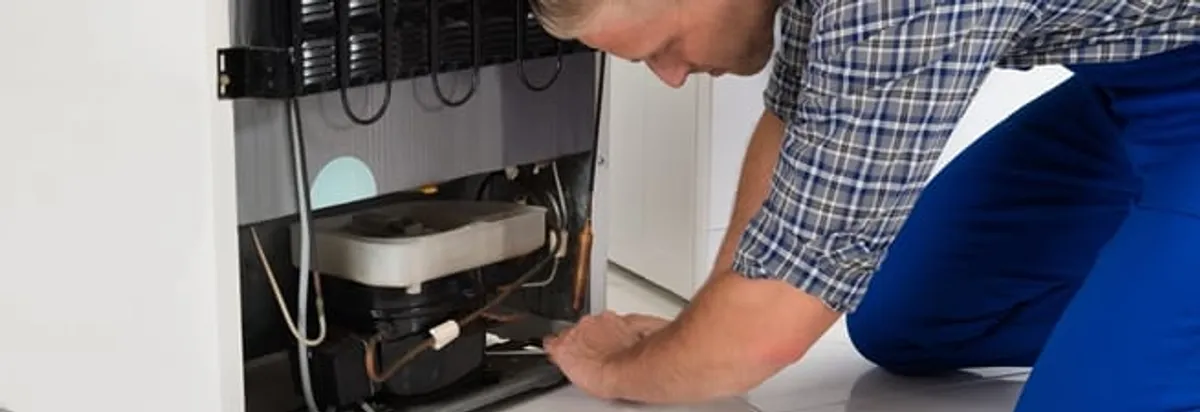 Refrigerator repair technician servicing the compressor and condenser area in Pittsburgh, PA